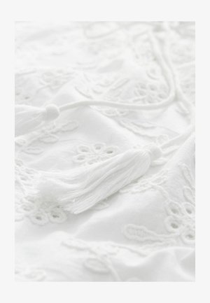 Hvidt stof med broderede blomsterdesigns og frynser. Teksturen er blød, med detaljerede indviklinger og en ensartet farve.