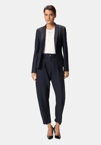 Completo a righe sottili blu navy con blazer sartoriale e pantaloni larghi. Il blazer presenta una chiusura con un solo bottone e tasche laterali.