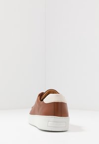 Bruna lädersneakers med vit gummisul mör och rund form, samt krämfärgad hälackcent. Har en minimalistisk design och diskret varumärkesdetalj.