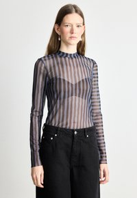 Top trasparente a maniche lunghe con strisce orizzontali scure e chiare, colletto alto e corpetto aderente. Abbinato a pantaloni neri a vita alta.
