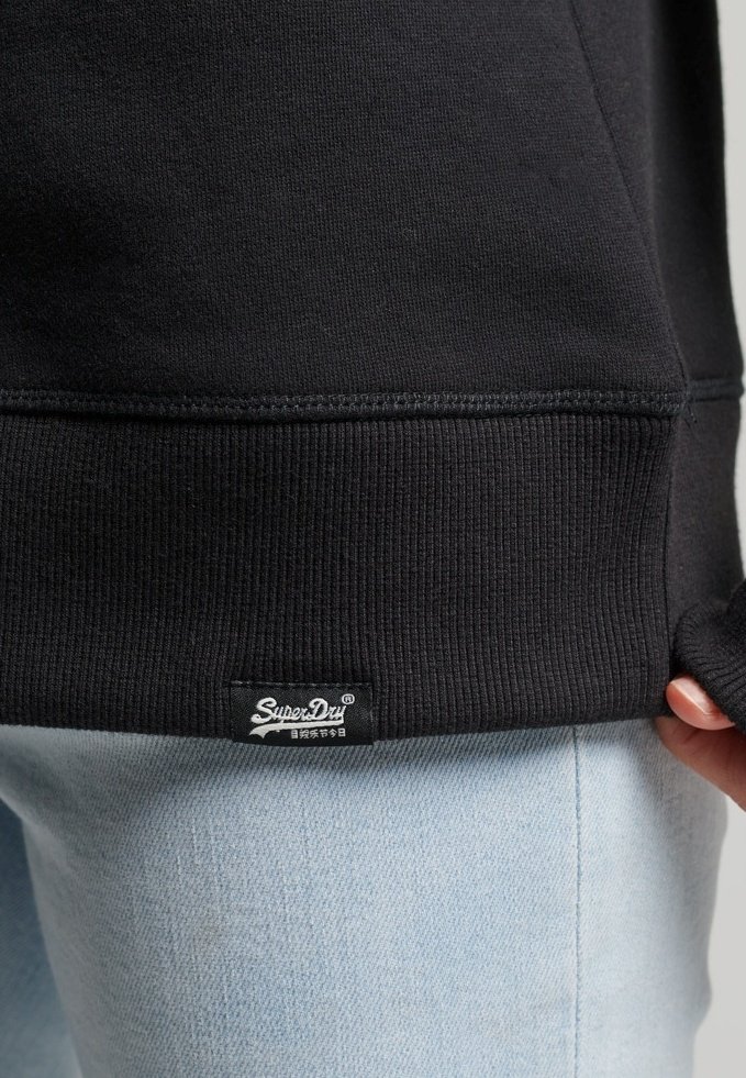 Sweat-shirt noir en tissu doux avec texture côtelée à l'ourlet, comportant une petite étiquette blanche avec la marque "SuperDry".