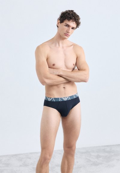 Schwarze Herren-Slips mit kontrastierendem Bund und Logo. Weicher Stoff in körpernaher Passform, der Konturen und Komfort hervorhebt.