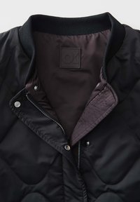 Veste matelassée noire avec un col côtelé, une fermeture éclair à l'avant dotée de boutons-pression, et une doublure intérieure lisse avec une étiquette de logo.