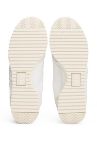 Baskets blanches avec des semelles texturées, présentant un motif strié, un tissu lisse et un accent de logo sur le côté, conçues pour un usage décontracté.