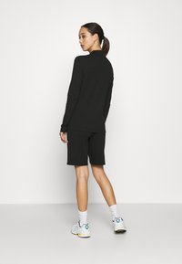Outfit composto da una maglietta nera a maniche lunghe e pantaloni corti, con una superficie liscia. Colore nero solido, design minimalista, abbinato a scarpe sportive.