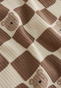 Brown and beige checkered fabric with ribbed texture featuring smiling bear faces within some squares.