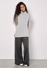 Grauer Pullover mit Kapuze und langen Ärmeln, kombiniert mit weit geschnittenen, strukturierten Schwarz- und Graumusterhosen. Weiße Schuhe vervollständigen das Outfit.