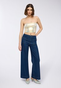 Złoty top bez ramiączek o gładkiej, lustrzanej fakturze; szerokie, ciemnoniebieskie dżinsy z kontrastowym przeszyciem i dwoma przednimi kieszeniami.