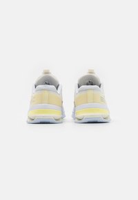 Białe i żółte buty sportowe z teksturowaną siateczkową cholewką, trwałą gumową podeszwą i wyraźnym paskiem na pięcie. Wyraźne logo po boku.