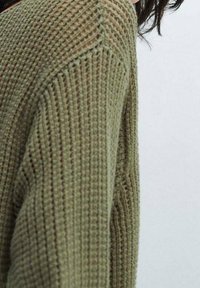 Gebreide trui in olijfgroen met een gestructureerd patroon, lange mouwen en een ontspannen pasvorm. Zichtbare naden en een subtiele ribbelafwerking.