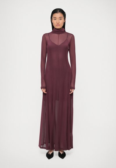Robe bordeaux à manches longues avec un col haut et un tissu transparent, présentant un corsage ajusté et une jupe fluide. Chaussures noires à bout pointu visibles.