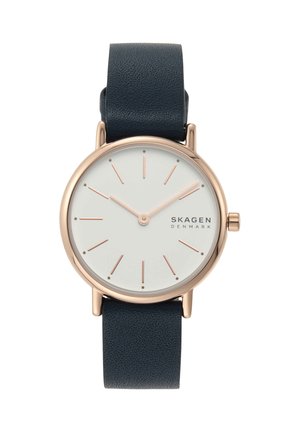 Kulaté bílé číselníky s růžově zlatými značkami a ručičkami, černý kožený řemínek a logo SKAGEN Denmark na pravé straně.