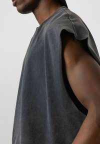 Grijze mouwloze shirt met een relaxte pasvorm, met ruwe randen bij de armsgaten en een zachte textuur. De stof heeft een subtiele, versleten uitstraling.