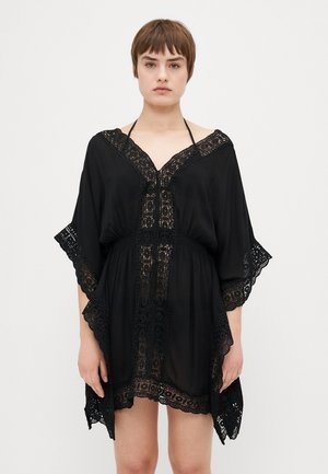 Czarny kaftan wykonany z lekkiego materiału, z koronkowym wykończeniem przy dekolcie i rękawach, o luźnym kroju i dekolcie w kształcie litery V.
