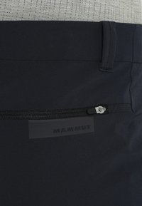 Pantaloni neri da esterno con tasca con zip, patch in gomma con il logo del marchio "Mammut" e un tessuto liscio e strutturato.