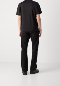 T-shirt nera a maniche corte abbinata a pantaloni neri slim-fit e scarpe nere. Il tessuto sembra liscio, con un design semplice e senza decorazioni.