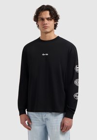 Zwarte longsleeve T-shirt met ronde hals, voorzien van witte geborduurde tekst op de borst en bedrukte accenten op beide mouwen. Gemaakt van katoen.