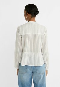 Vit, randig blus med långa ärmar, rynkad midja och en avslappnad passform, parat med ljus denimjeans.