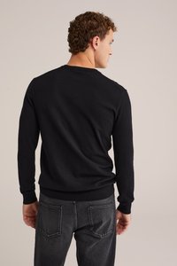 Črna dolga majica s dolgimi rokavi in krožnim izrezom, mehka pletenina, rebrast rob in manšete, v kombinaciji s temno sivo denim hlačami z zadnjimi žepi.