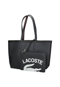 Bolso tote negro con asas texturizadas, que incluye un pouch negro desmontable con un logo blanco de Lacoste y un gráfico de cocodrilo. Material liso.