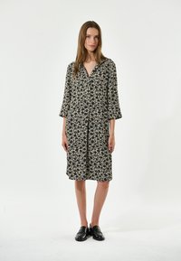 Blumenkleid in Creme und Schwarz, mit durchgehender Knopfleiste, Kragen und dreiviertellangen Ärmeln, aus leichtem Stoff gefertigt.