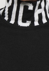 Černý žebrovaný pletený rolák s bílým kontrastním logem na límci, vyrobený z texturovaného a pružného materiálu.