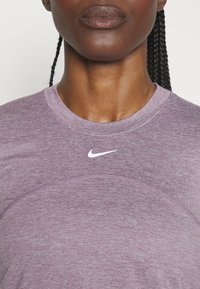 Rundhalset, kortærmet sportstrøje i meleret lilla stof med glat tekstur. Har et hvidt Nike-logo på brystet.
