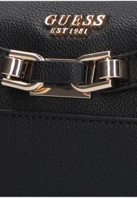 Black leather handbag featuring textured surface, gold hardware detail, and the "GUESS" logo embossed on the flap. Stylish closure accent.