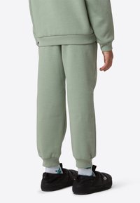 Light green cotton sweatshirt and matching sweatpants with ribbed cuffs and waistband, paired with black slip-on shoes and patterned socks.