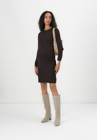 Abito a maglia marrone a coste con maniche lunghe, abbinato a stivali con tacco alti fino alla coscia beige e una borsa a tracolla beige chiaro.
