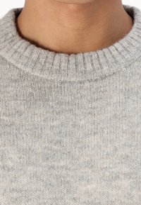 Ljusgrå stickad tröja med ribbad rund halsringning. Mjuk textur och subtilt mönster synligt i tyget.