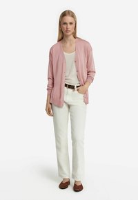 Ljust rosa cardigan med knappar, bärs över en vit topp och matchas med vita byxor. Bruna skor fulländar outfitten. Slät textur, avslappnad passform.