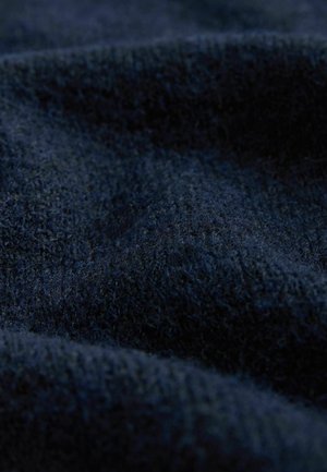 Námořnická texturovaná látka ukazující měkký, chlupatý materiál s různou hloubkou, vytvářející vlnitý vzor na povrchu.