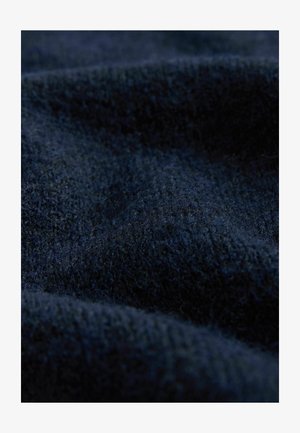 Námořnická texturovaná látka ukazující měkký, chlupatý materiál s různou hloubkou, vytvářející vlnitý vzor na povrchu.