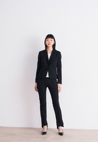 Black tailored suit with structured blazer and slim trousers, paired with a white top. Smooth fabric, minimalistic design, and classic fit.