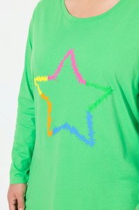 Grön långärmad skjorta med en mångfärgad stjärndesign i rosa, gult, orange och blått, med en fluffig, zigzag-textur.
