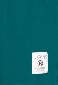 Sinine puuvillane T-särk, millel on valge brändi etikett, millel on mustalt kirjas "LEVI'S ® 1873". Sile tekstuur ja vabaaja disain.