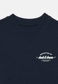 Μπλε ναυτική μπλούζα με στρογγυλή λαιμόκοψη και κοντά μανίκια. Φέρει λευκή κ αι πράσινη εκτύπωση κειμένου που λέει "Ορισμός του Jack & Jones."