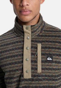 Πουλόβερ με ψηλό γιακά, κλείσιμο με κουμπιά, μικτή υφή. Διαθέτει υφασμάτινο σχέδιο σε καφέ και γκρι αποχρώσεις, με τσέπη και patch με το λογότυπο.