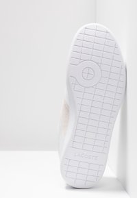 Semelle blanche de basket avec motif en grille, dessin circulaire d'adhérence près du centre, et nom de marque "LACOSTE" embossé au talon.