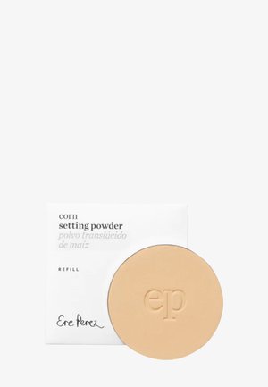 Poudre fixante à base de maïs dans un boîtier rond beige. Le produit porte un logo "ep" en relief. Une boîte blanche présente un texte noir détaillant le produit.