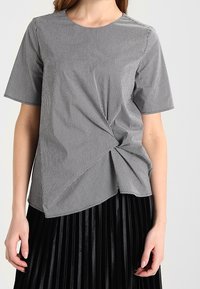 Top a maniche corte in motivo check nero e bianco, con dettaglio frontale annodato e vestibilità rilassata. Tessuto testurizzato, design casual.