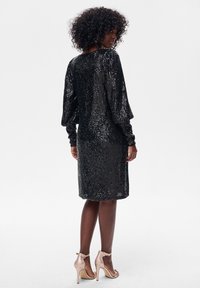 Czarna sukienka z cekinami z długimi bufkami i dopasowaną sylwetką, z pionowymi paskami cekinów i długością za kolano.