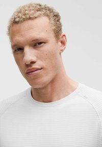 Jasnoszara koszulka sportowa z okrągłym dekoltem, z teksturowanym wzorem i dopasowanym krojem. Widoczne szwy i subtelne prążkowanie na ramionach.