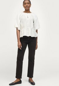 Blusa blanca con textura, mangas abullonadas y escote en forma de ojo de cerradura, combinada con jeans oscuros y bailarinas negras.