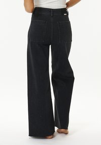Vaqueros de mezclilla negros de cintura alta con piernas anchas, que presentan grandes bolsillos traseros y dobladillos deshilachados. Textura suave y diseño de cinturilla plana.