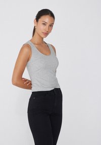 Šedý bavlněný top bez rukávů s kulatým výstřihem, úzkým střihem a hladkou texturou, spárovaný s černými skinny džíny s předními kapsami.