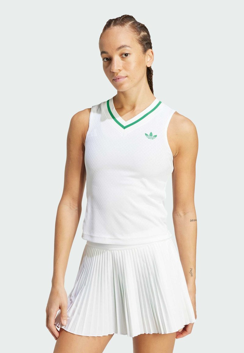 Camiseta deportiva blanca sin mangas con escote en forma de V y cuello a rayas verdes, combinada con una falda blanca plisada. La camiseta presenta un pequeño logo verde.