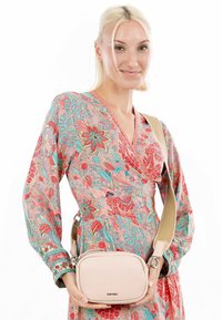 Borsa a tracolla rosa chiaro con una texture di pelle liscia, forma ovale e tracolla regolabile, tenuta da un modello che indossa un vestito con motivo floreale.