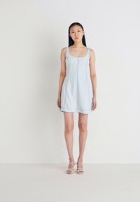 Light blue denim dress with a sleeveless design, round neckline, side seams, and a slightly flared silhouette. Pair of strappy sandals.